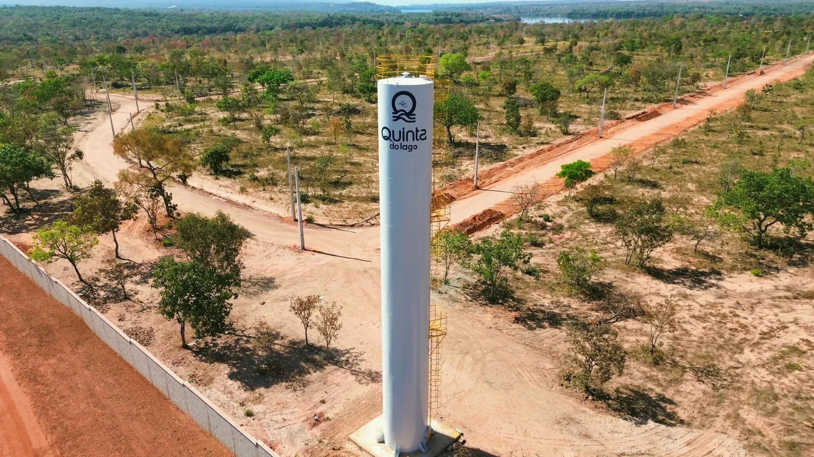 Reservatório de água do Quinta do Lago, uma torre branca com o símbolo do condomínio, entre as ruas de terra