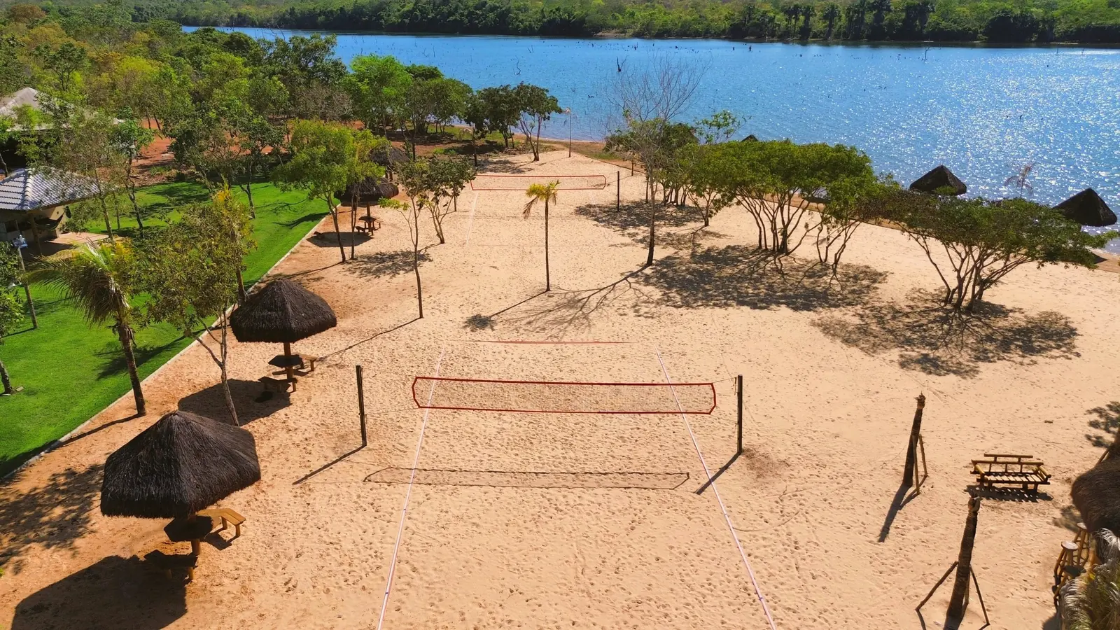 Rede de vôlei na areia do Quinta do Lago, entre árvores e quiosques, com o lago ao fundo